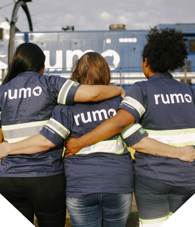 Três mulheres abraçadas, de costas, usando o uniforme da Rumo | Rumo