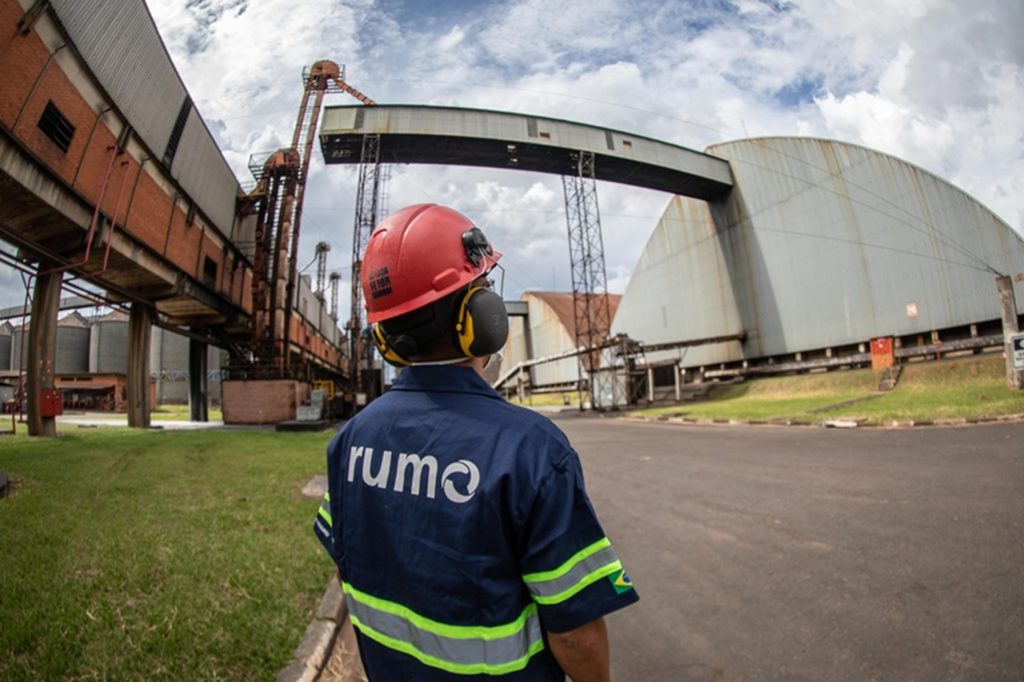 Homem de costas com o uniforme da Rumo olhando para um galpão