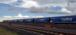 Trem de carga azul da Rumo em via férrea sob céu nublado.