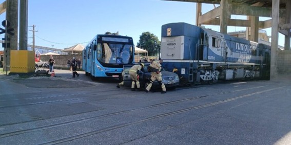 Ônibus azul e trem parados próximos a carro cinza em via férrea.