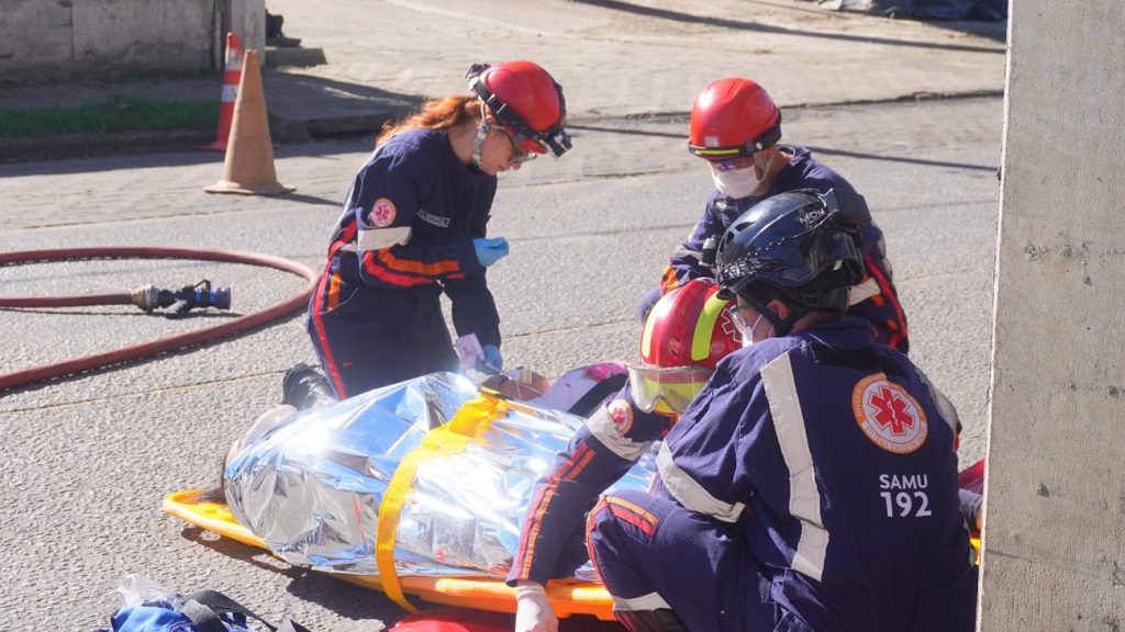 Equipe de resgate com capacetes e uniformes atendendo pessoa em maca.