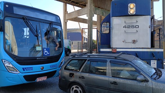 Ônibus azul e trem parados próximos a carro cinza em via férrea.
